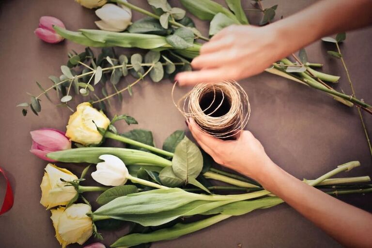 Person grabbing the ends of a string while arranging flowers that are laid on a table