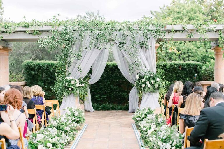 Center aisle of a wedding venue designed with white flowers and green leaves