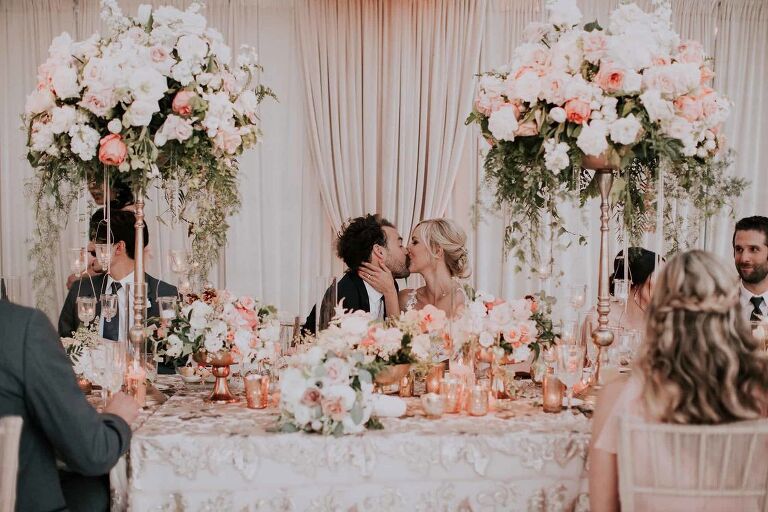 Bride and groom kissing while sitting on their table at a wedding reception